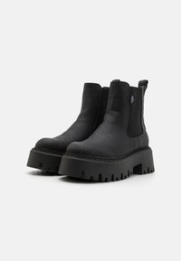 Bottines Chelsea noires en cuir synthétique texturé, avec des panneaux latéraux élastiques, une languette de traction et une semelle épaisse et dentelée.