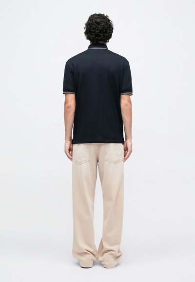 Μπλε ναυτικό πόλο με κλασικό γιακά και λευκή διακόσμηση, συνδυασμένο με α νοιχτό μπεζ παντελόνι φαρδιάς γραμμής με μπαλώματα στις τσέπες και άνετη εφαρμογή.