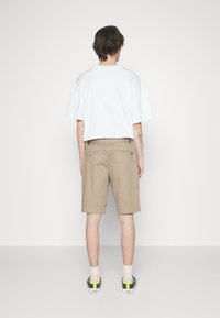 T-shirt blanc surdimensionné, shorts beiges et baskets vertes avec des accents jaunes. Texture unie avec un design minimaliste. Vue de dos.