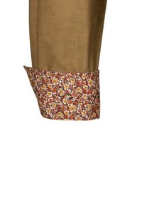 Camicia marrone con un polsino a fantasia floreale che presenta fiori gialli, arancioni e bianchi su uno sfondo scuro. Tessuto dalla consistenza liscia.