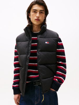 Schwarze Steppweste mit hohem Kragen über einem rot-, weiß- und blau gestreiften Pullover. Die Weste hat einen Reißverschluss und ist aus einem glatten Stoff gefertigt.
