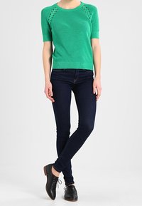 Grøn kortærmet striktrøje med hulmønster på skuldrene, parret med mørkeblå skinny jeans og sorte snørebåndssko.