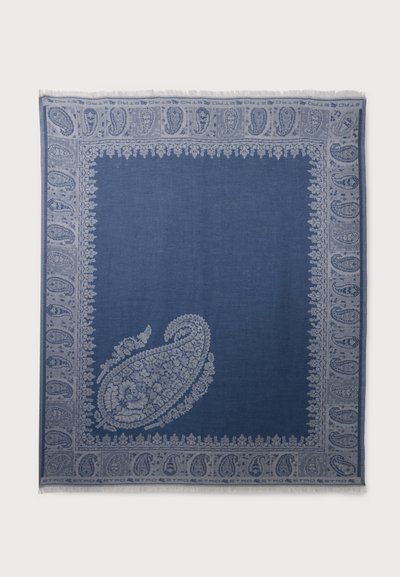 Textile rectangulaire bleu avec des motifs paisley clairs le long de la bordure et un grand motif paisley complexe près d’un coin.