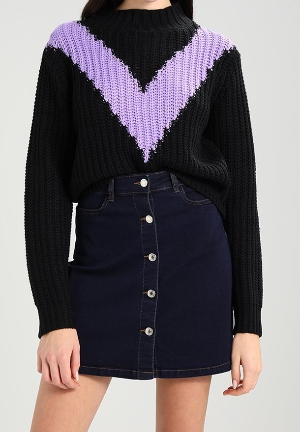Schwarzer Strickpullover mit einem violetten V-Muster auf der Brust, kombiniert mit einem dunklen Jeansrock mit Knöpfen vorne und einer taillierten Silhouette.