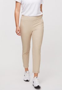 Beige elastické kalhoty ke kotníkům s hladkým pasem a bočními kapsami, spárované s bílými teniskami.