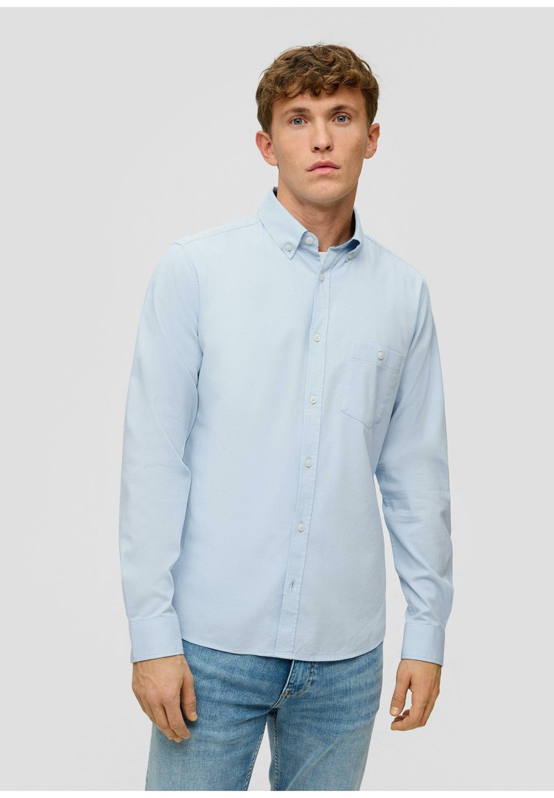 Camicia azzurro chiaro a maniche lunghe con bottoni in tessuto di cotone. Presenta una piccola tasca sul petto e un colletto classico. Abbinata a jeans di denim.