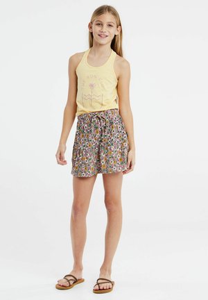 Débardeur jaune avec un motif de palmiers, associé à une jupe rose à motifs floraux avec une taille à cordon. Porté avec des sandales à lanières marron.