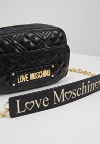Svart kviltad axelväska med en guld "LOVE MOSCHINO" platta, som har en guld kedjerygg och en avtagbar rem med logotypbokstäver.