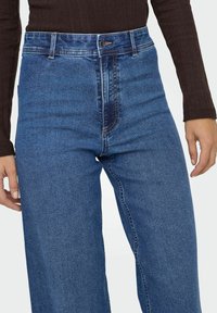 Traperice visoka struka od trapera, s ravnim krojem nogavica, suptilnim izblijedjelim detaljima i kontrastnim šavovima na džepovima.