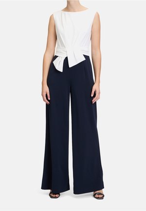 Biały top bez rękawów z przednim skręceniem oraz granatowe spodnie z szerokimi nogawkami, tworzące elegancką sylwetkę. Gładka tkanina, minimalistyczny design.