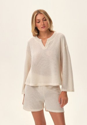 White, knitted loungewear set featuring a loose-fitting long-sleeve top with a V-neck and matching shorts with an elastic waistband.