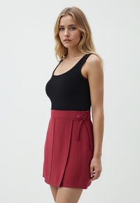Zwarte geribbelde tanktop met brede banden, gecombineerd met een hooggeknipte, knie-lange rode rok met plooien en een strikaccent in de taille.