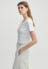 T-shirt �à manches courtes, court, dans un motif moucheté gris clair avec un col rond et des détails en chaîne argentée. Assorti à un pantalon clair taille haute.