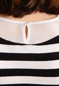 Svart och vit randig skjorta med en genomskinlig vit yoke. Har en knappstängning och en liten nyckelhålsöppning på ryggen. Mjuk tygtextur.