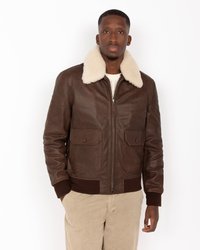 Chaqueta bomber de cuero marrón con un cuello de borreguito color crema, cremallera frontal y dos bolsillos en el pecho. Puños y dobladillo de canalé. Textura suave.