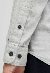 Lichtgrijze button-up shirtmanchet met twee zwarte knopen, subtiele textuur en gestikte details langs de randen.