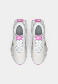 Λευκά αθλητικά παπούτσια Nike με διχτυωτό πάνω μέρος, ροζ λεπτομέρειες στη φτέρνα και στην γλώσσα, γκρι εσωτερικό και χρυσό λογότυπο swoosh στο πλάι.