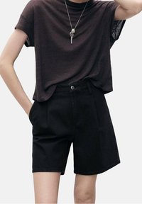 Shorts de mezclilla negra con un ajuste entallado, que presentan un cierre delantero con botón y bolsillos laterales, combinados con una camiseta de manga corta marrón oscuro.