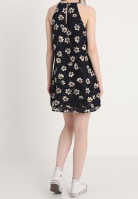 Czarna sukienka w kwiaty z dekoltem halter, zdobiona białymi i kremowymi kwiatami. Wykończona dekoltem w kształcie łezki i zwiewną fakturą.