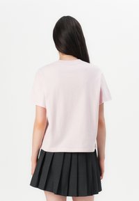 Lys rosa t-skjorte med kort erm og rett snitt, sammen med et svart plisserte skjørt.