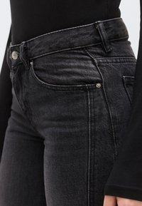 Fekete farmernadrág magas derékkal, klasszikus öt zsebes kivitel, finom varrási részletekkel és enyhén kifakult textúrával.