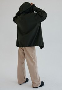 Ciemnozielona kurtka z kapturem o luźnym kroju, teksturowana, z ściągniętym dołem, noszona na jasnobeżowych, szerokich spodniach i czarnych butach.