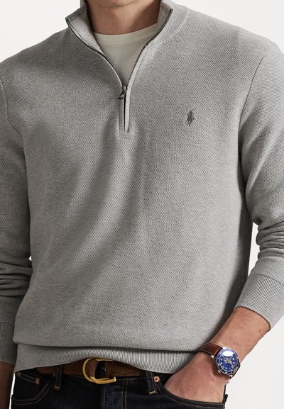 Pullover cinza de malha com gola de fecho de correr até um quarto, apresentando um padrão texturizado e um pequeno logo no peito. Usado sobre uma camisa creme.