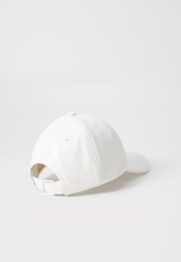 Căciulă albă din piele, cu vizor curbat, curea ajustabilă în spate și orificii de ventilație pe fiecare parte. Textură netedă, design minimalist.