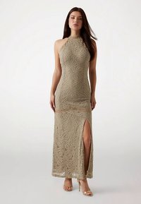 Trägerloses, figurbetontes langes Kleid aus strukturiertem beigen Spitzenstoff mit seitlichem Schlitz, versehen mit filigranen Mustern und offenen Strickakzenten.