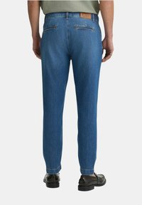 Jeans in denim blu con una vestibilità a gamba dritta, dotati di due tasche posteriori con cerniere, un'etichetta in pelle marrone sulla vita e una texture leggermente scolorita.