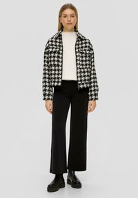 Zwart-wit houndstooth-gepatenteerde jas met een kraag, gecombineerd met een witte trui en zwarte wijde broek. Chunky zwarte enkelboots.