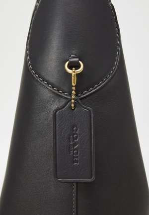 Schwarze Leder-Hobo-Tasche mit breitem Träger, dezentem Logo vorne und kleinem hängenden Anhänger mit Kette auf einfarbigem Hintergrund.