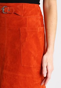 Ruskohvärvi nahast seelik, millel on vööga talje, eesmine tasku ja sile tekstuur. Disain sisaldab puhtaid õmblusi ja minimalistlikke aktsente.