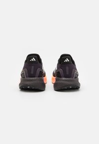 Baskets de sport noires et violettes avec une tige texturée, dotées de trois bandes blanches et d'un intercalaire orange. Semelle extérieure en caoutchouc avec un motif de relief.