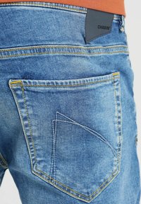 Vaqueros de mezclilla azul claro con costuras visibles, con un diseño único de bolsillo y una etiqueta de cuero con la marca en la cinturilla.