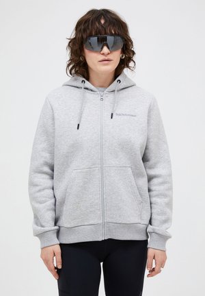 Graue Zip-Hoodie mit Kordelzügen, Fronttaschen und gerippte Bündchen. Markenlogo auf der Brust. Modell trägt übergroße schwarze Sonnenbrillen.