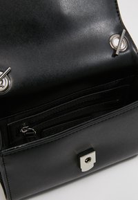 Borsa a mano in pelle nera con texture liscia, dotata di accessori in argento, una tasca interna con zip e una chiusura sicura a scatto.