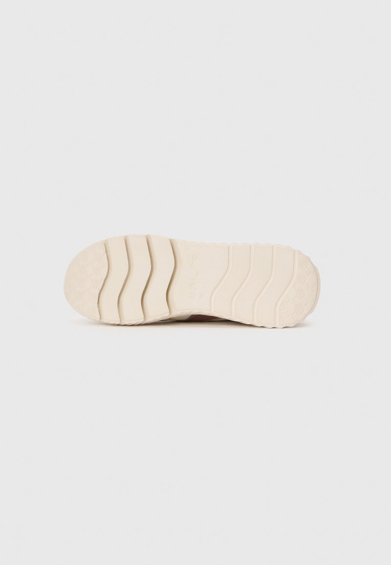 Suola di sneaker in gomma beige con un motivo testurizzato, caratterizzata da scanalature prominenti e un'impronta del logo vicino al tallone.