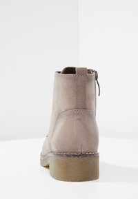 Šedá semišová kotníková bota s kulatou špičkou, bočním zipem a texturovanou podrážkou. Obsahuje šitý šev a elastický prvek na patě.