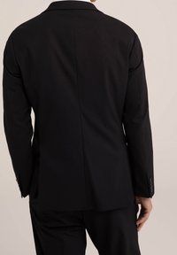 Svart skräddarsydd kavaj med slagkrage, enkel sprund bak, strukturerad tyg och knappade manschetter. Bakifrån som visar passform och struktur.