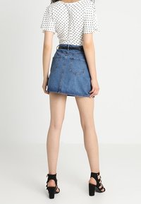 Džínová mini sukně se mírně rozšířeným střihem, modré barvy a se čtyřmi viditelnými kapsami. Doplněná polkadotovou blůzou a černými podpatky.