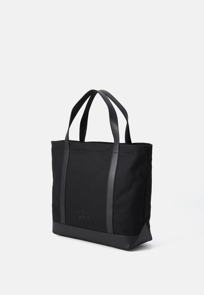 Bolsa de tela negra con acentos de cuero negro, fondo plano, asas dobles y detalle del logo embosado en el frente.