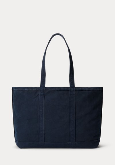 Grand sac fourre-tout en tissu bleu marine avec deux longues anses et une couture simple sur un fond clair uni.