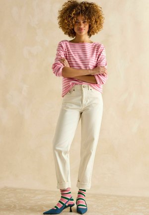 Gestreiftes rosa und weißes Langarmshirt, cremefarbene High-Waist-Jeans, mehrfarbige gestreifte Socken, blaue spitze Absatzschuhe.