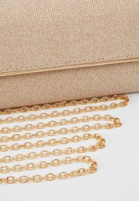 Kabelka v barvě šampánku vyrobená z látky s texturovaným povrchem. Disponuje zlatým řetízkem s kulatými články.