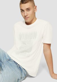 Witte katoenen t-shirt met een vervaagd grafisch ontwerp met de tekst "VISION" en stadsnamen, gecombineerd met blauwe spijkerbroek.