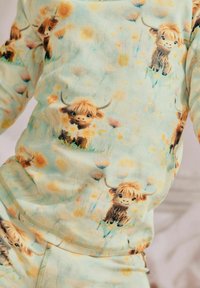 Fleece pyjamasoverdel i lys mintgrøn med tegneserie Highland køer og blomsterprint. Blødt stof med en afslappet pasform og rund halsudskæring.