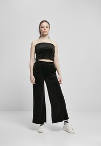 Bandeau en velours noir court associé à un pantalon large en velours noir. Le modèle porte des baskets blanches et des chaussettes rayées.