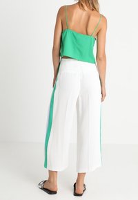 Top court vert à fines bretelles associé à un pantalon large blanc avec des accents verts sur les côtés. La tenue présente une texture lisse et une coupe décontractée.