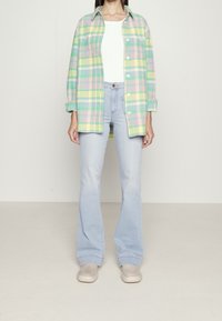 Chemise à carreaux légère dans les tons vert, rose et jaune, style boutonné, associée à un jean évasé bleu clair et des baskets beiges.
